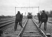167436 Afbeelding van wegwerkers van de N.S. tijdens het lossen van spoorstaven op de spoorlijn nabij Putten.